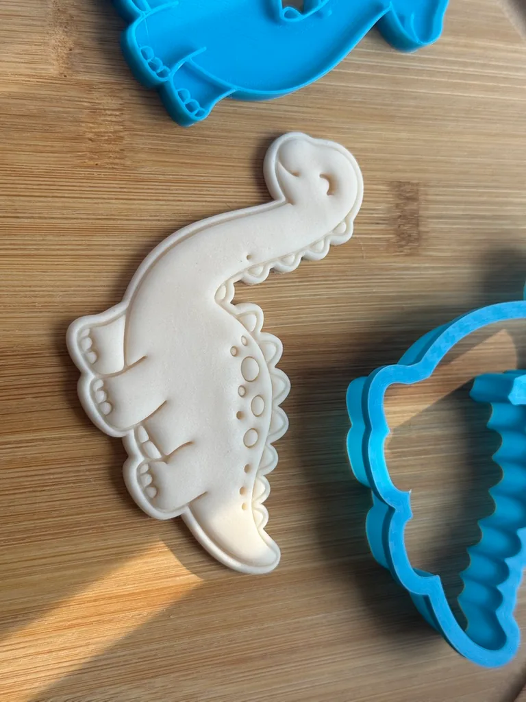 3D printed dinosaur cookie cutter beside the embossed fondant shape it makes