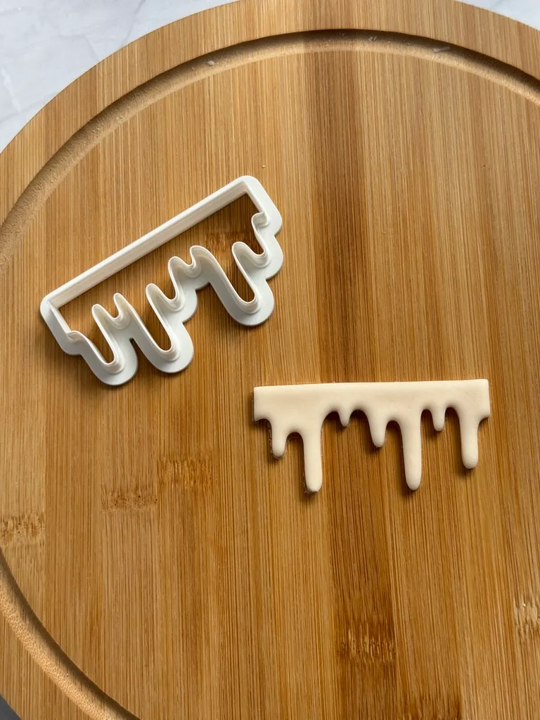 White drip cutter and the fondant drip edge it cuts, on a wooden board