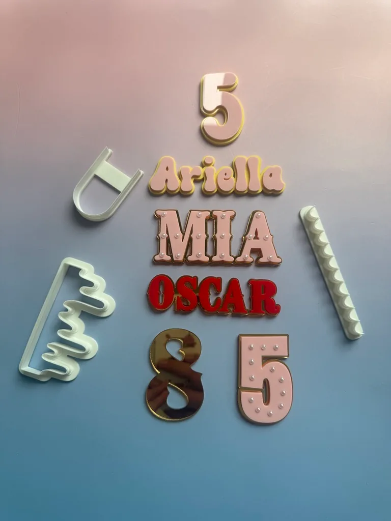 A group of layered name and number toppers with pearl detailing beside fondant cutters