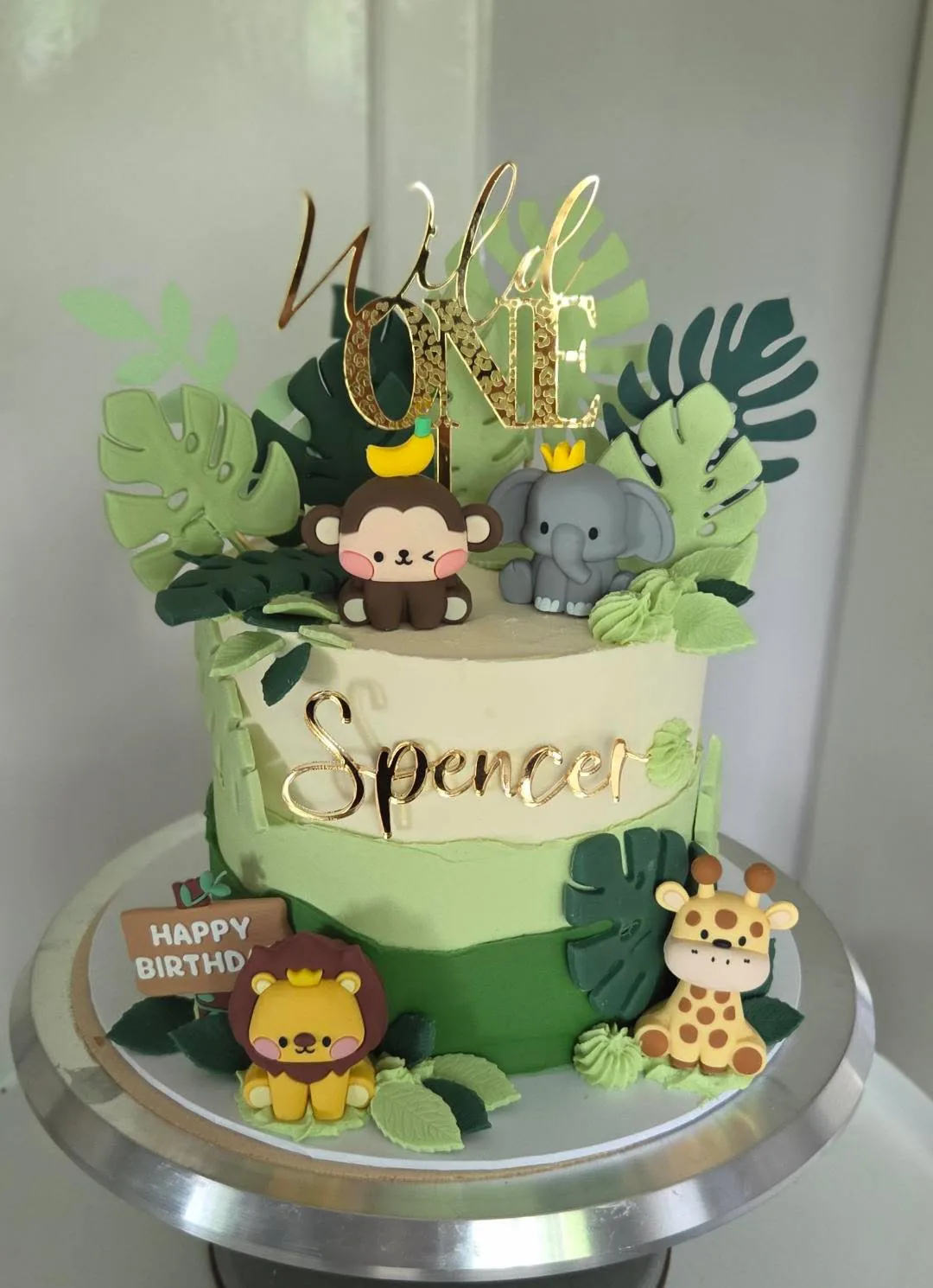 Green jungle cake with a gold Wild One topper and the name Spencer